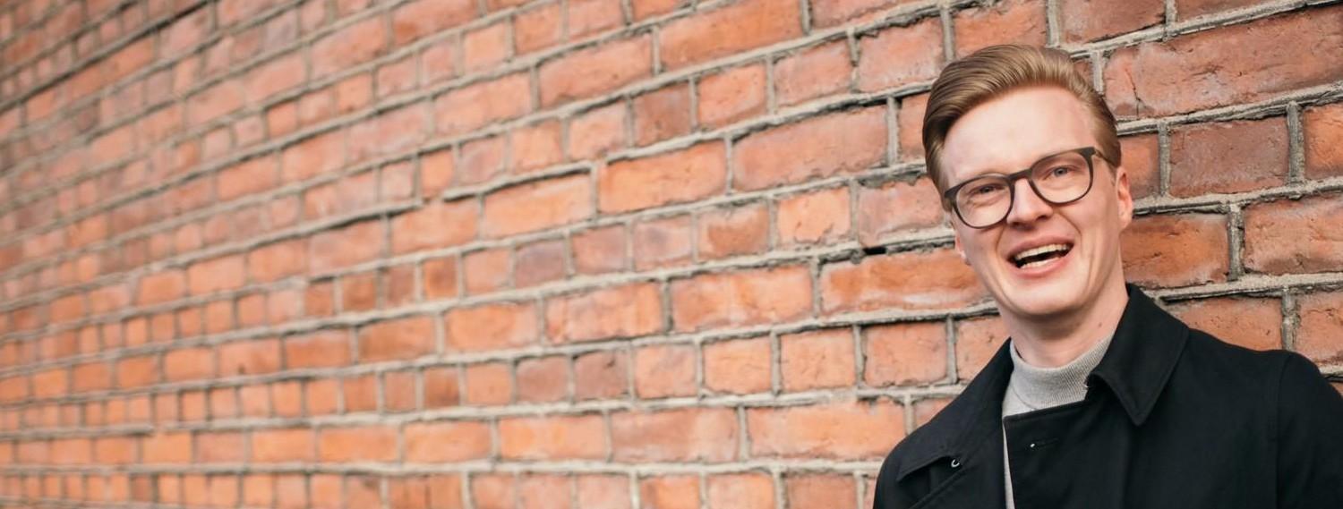 A smiling man standing in front of a red brick wall