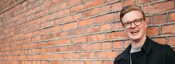 A smiling man standing in front of a red brick wall