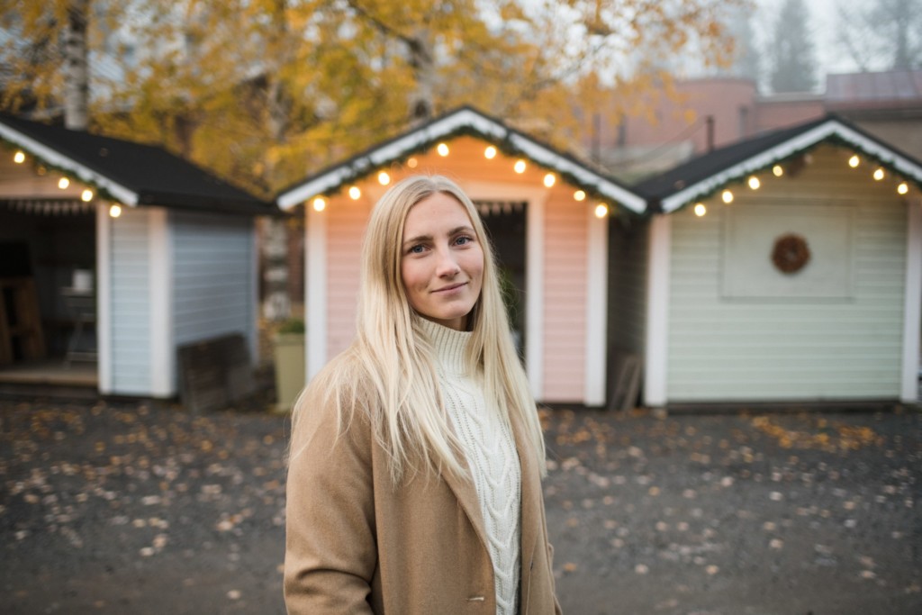 Woman stands outside, small colourful cottages in the background