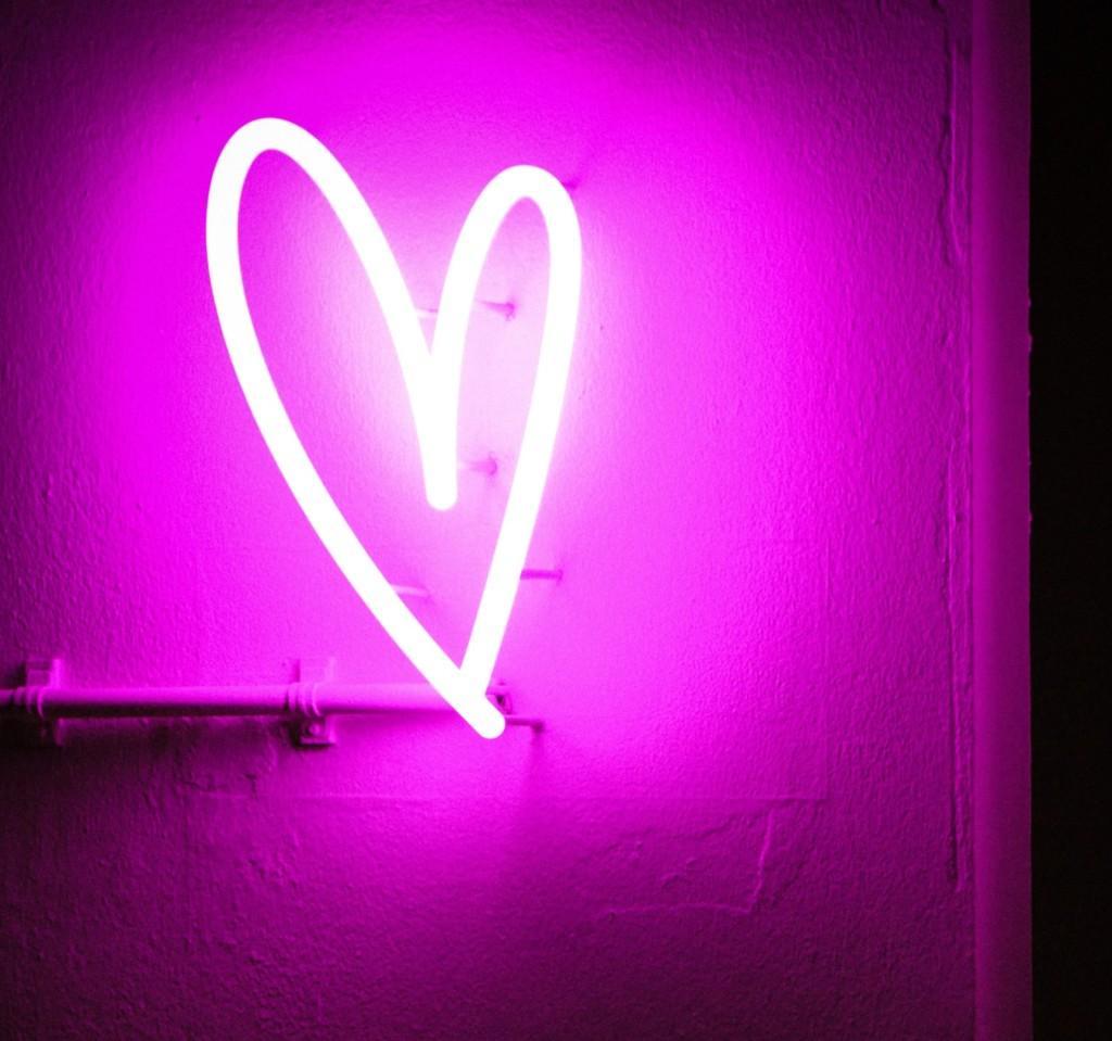 A heart-shaped, purple neon light, hanging on a wall.