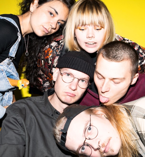 A group of five young people in different positions, in front of a yellow background