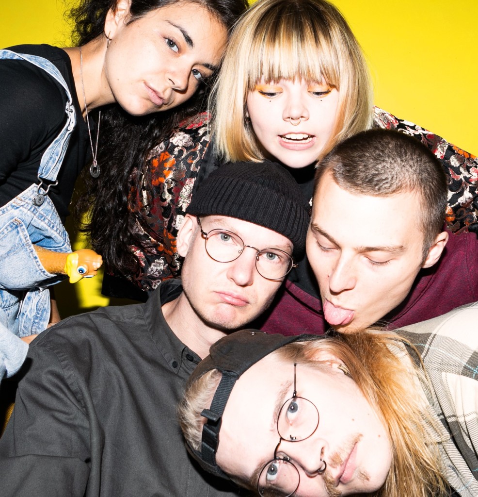 A group of five young people in different positions, in front of a yellow background