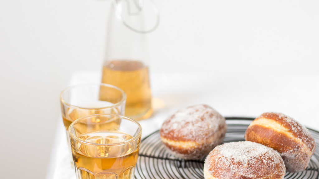 Simaa laseissa ja pulloissa, pyöreitä sokerimunkkeja lautasella.