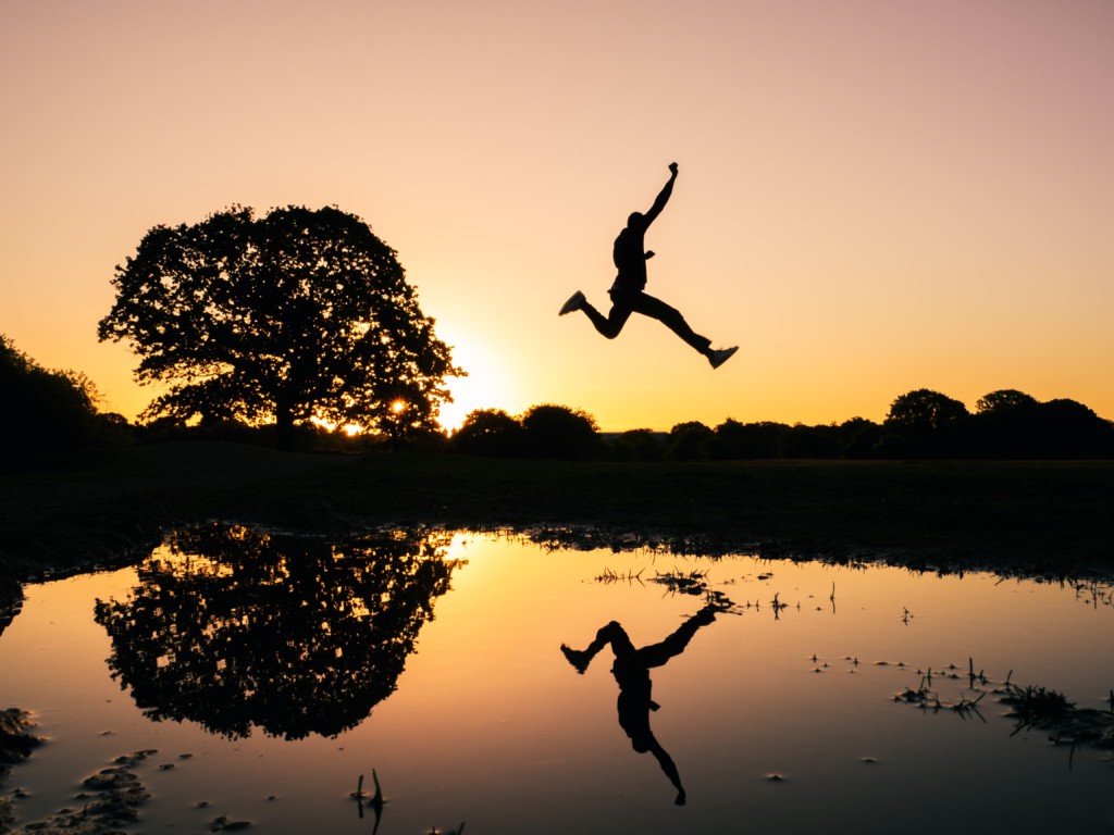 A person jumps over a pond at sun set.
