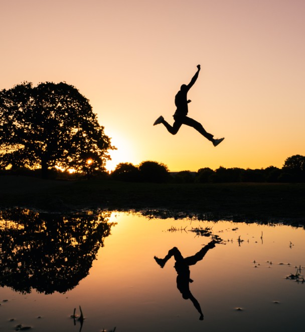 A person jumps over a pond at sun set.