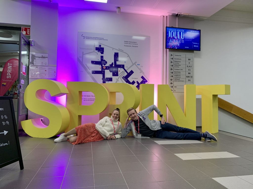 Two people lying on their sides. Huge yellow letters and lights in the background.