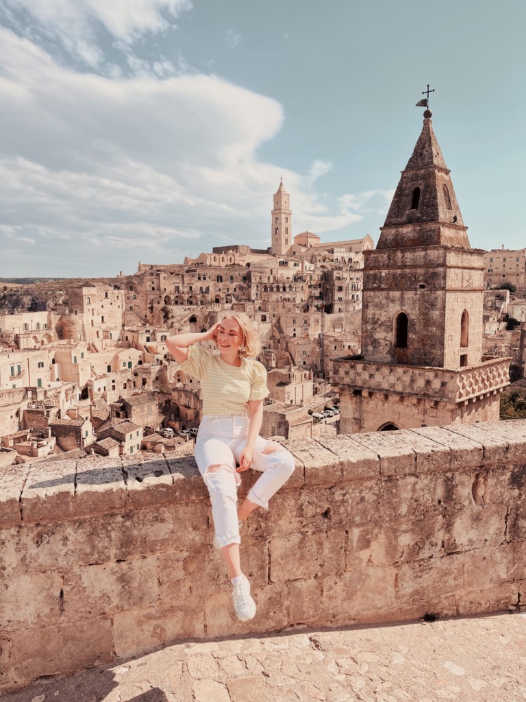 Saara sitting on a wall in Matera, with the old town in the background.