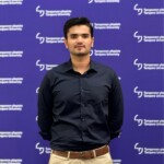 Haseeb seisoo valokuvausseinän edessä. Haseeb is standing in front of a photograph wall.