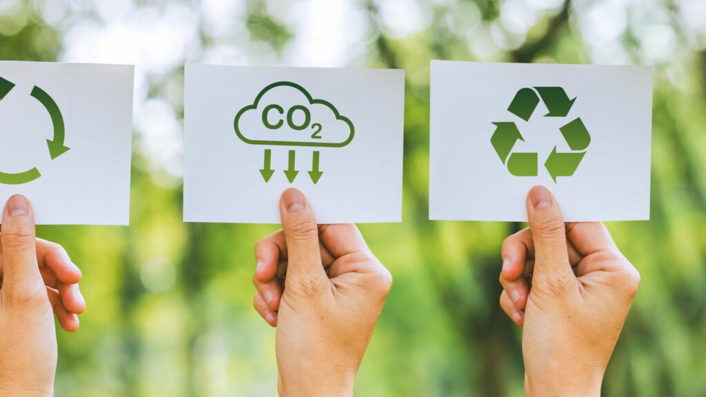 Three hands holding sustainability-related cards in the air.